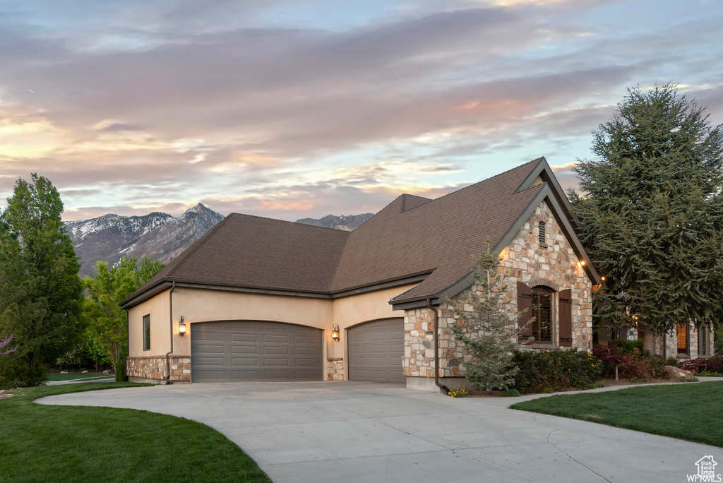 View of front facade with a garage, a mountain view, and a lawn