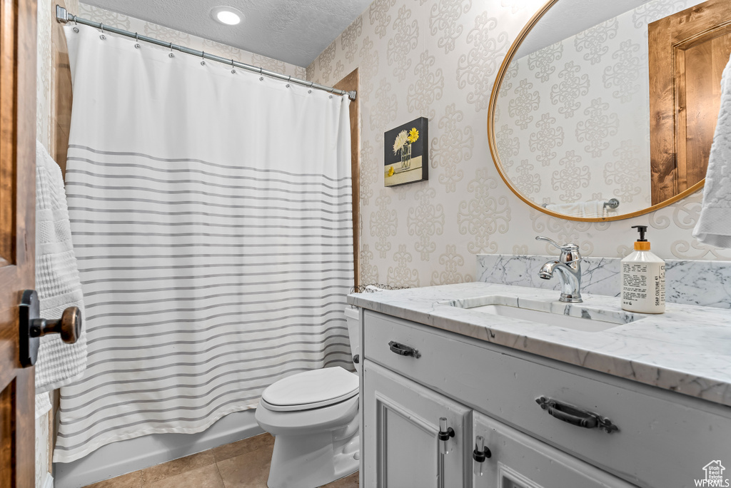 Full bathroom with toilet, tile floors, vanity, a textured ceiling, and shower / tub combo with curtain