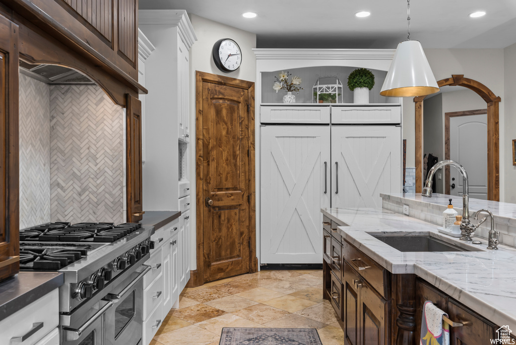 Kitchen featuring decorative light fixtures, range with two ovens, tasteful backsplash, white cabinetry, and sink