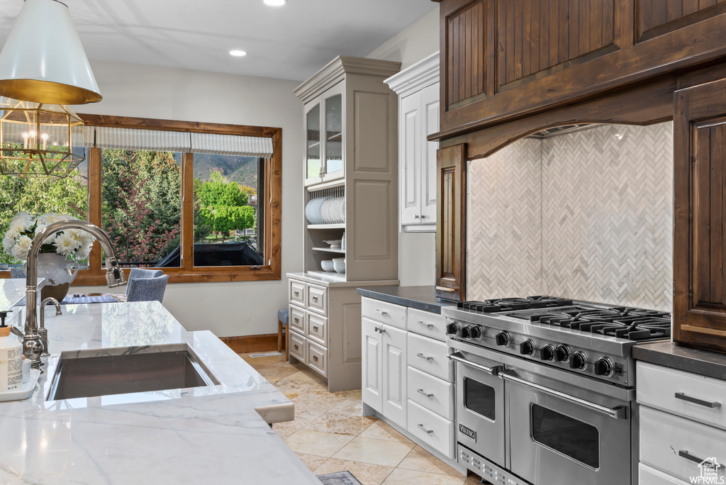 Kitchen with light stone counters, light tile flooring, white cabinetry, double oven range, and sink