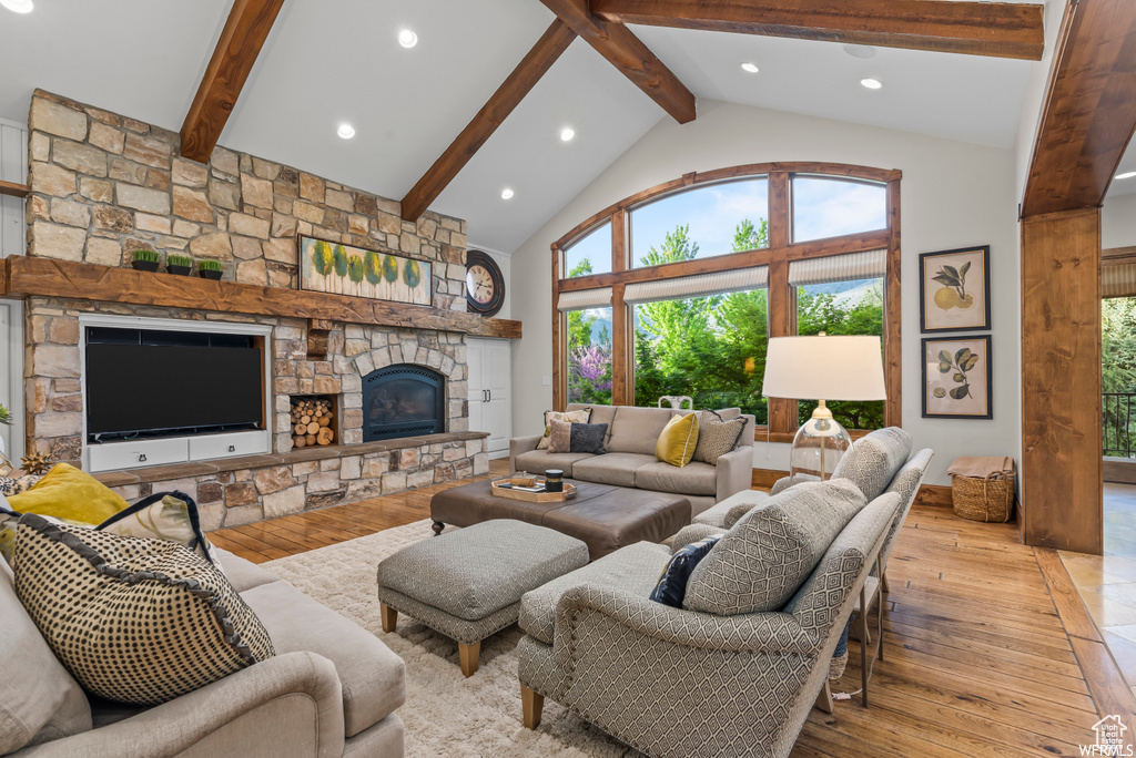 Living room featuring a stone fireplace, high vaulted ceiling, beamed ceiling, and light wood-type flooring