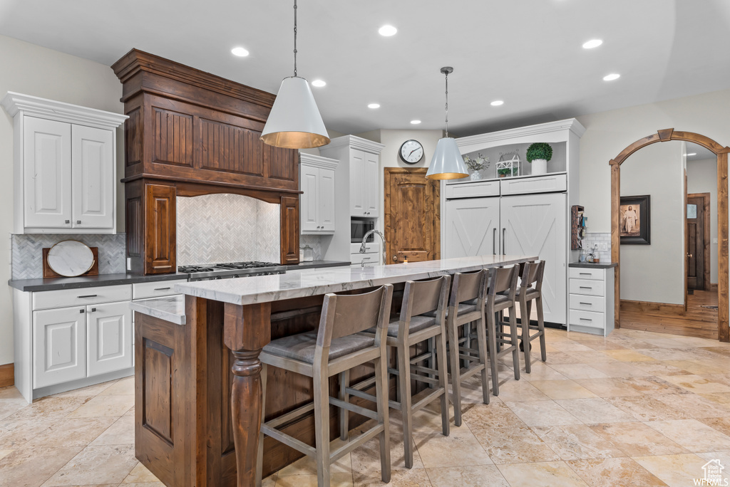 Kitchen with an island with sink, light stone counters, pendant lighting, tasteful backsplash, and light tile floors