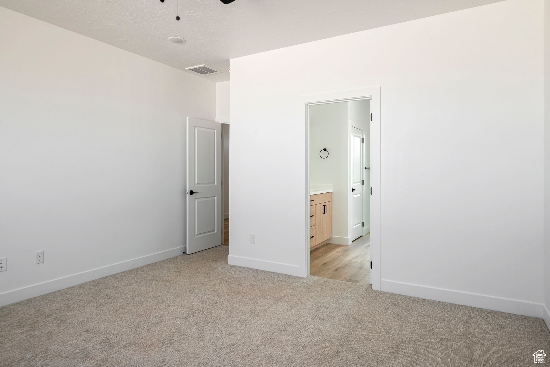 Unfurnished bedroom with light carpet, ensuite bathroom, and ceiling fan