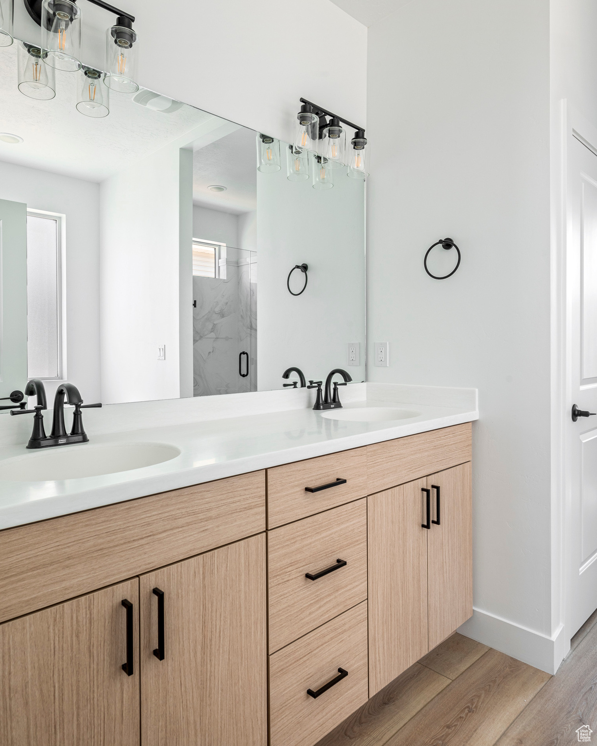 Bathroom featuring hardwood / wood-style flooring, a shower with door, and dual bowl vanity