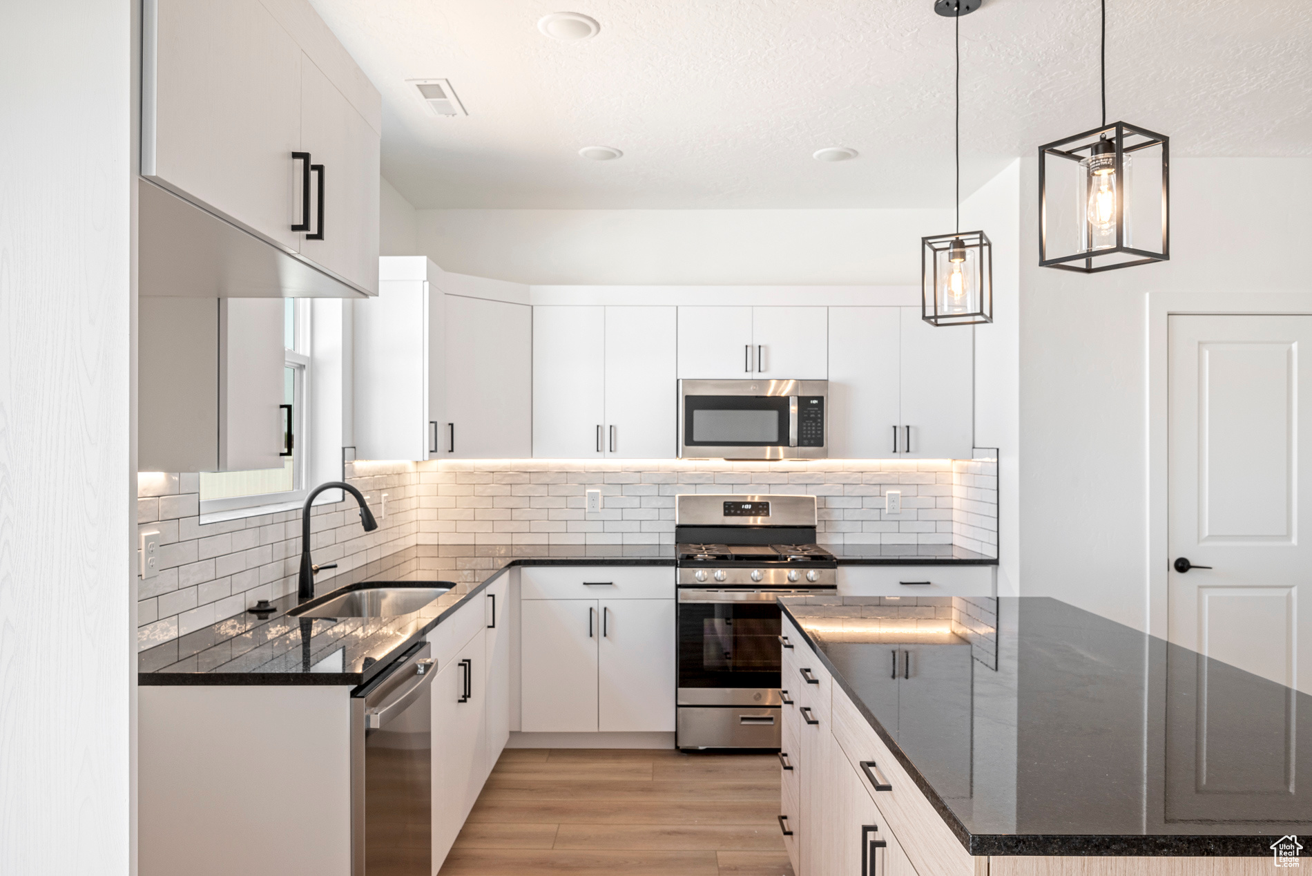 Kitchen with decorative light fixtures, tasteful backsplash, white cabinets, appliances with stainless steel finishes, and light hardwood / wood-style flooring