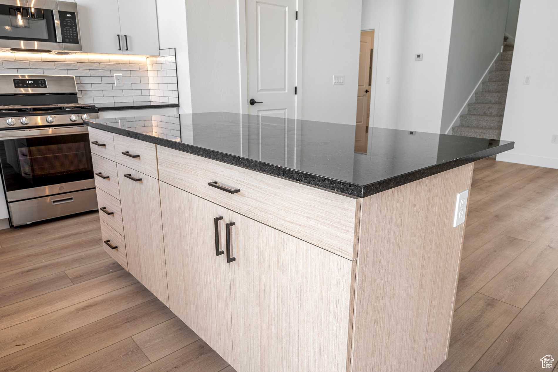 Kitchen with light brown cabinets, light wood-type flooring, backsplash, a center island, and appliances with stainless steel finishes