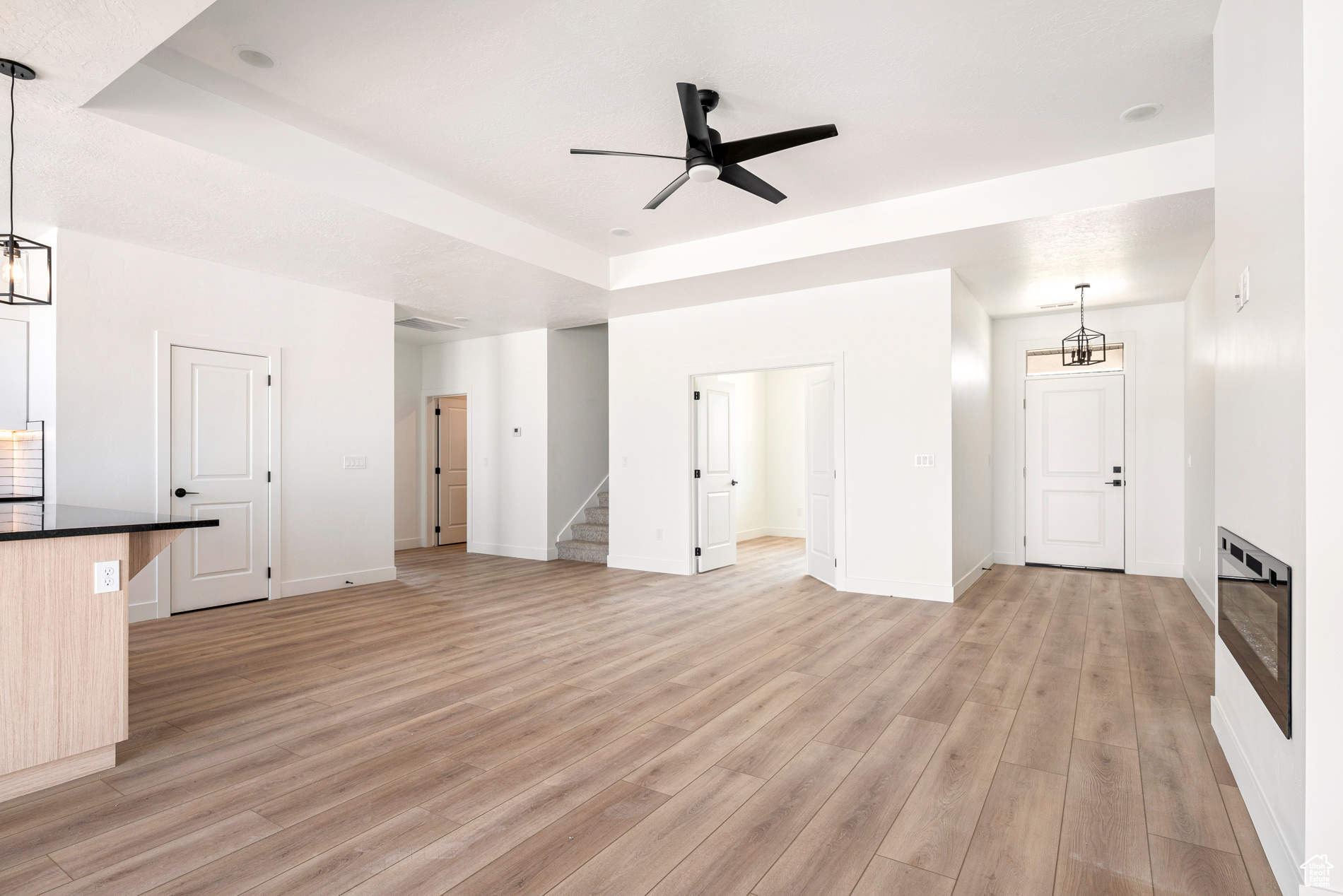 Unfurnished living room featuring ceiling fan with notable chandelier, a raised ceiling, and light hardwood / wood-style floors