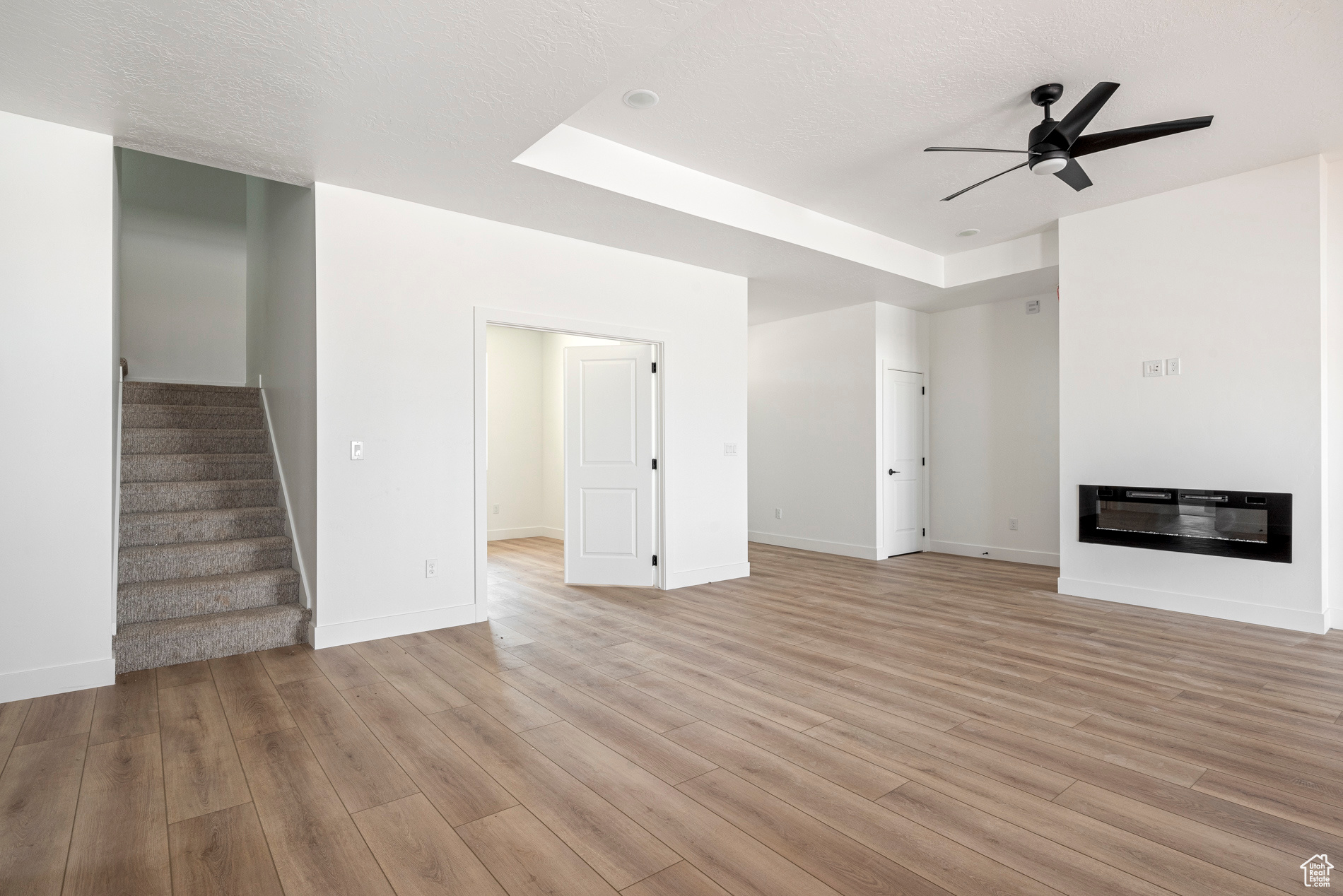 Unfurnished living room featuring light hardwood / wood-style floors, ceiling fan, and a raised ceiling