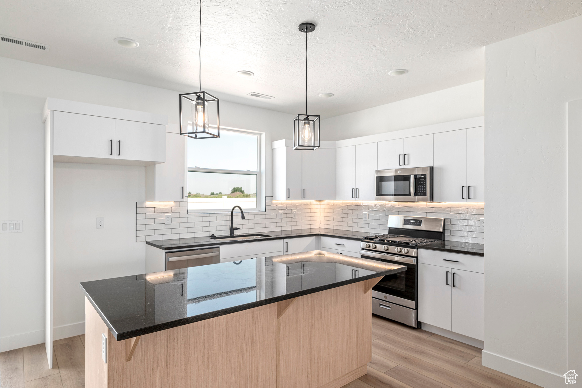 Kitchen with stainless steel appliances, white cabinets, sink, light hardwood / wood-style floors, and a center island