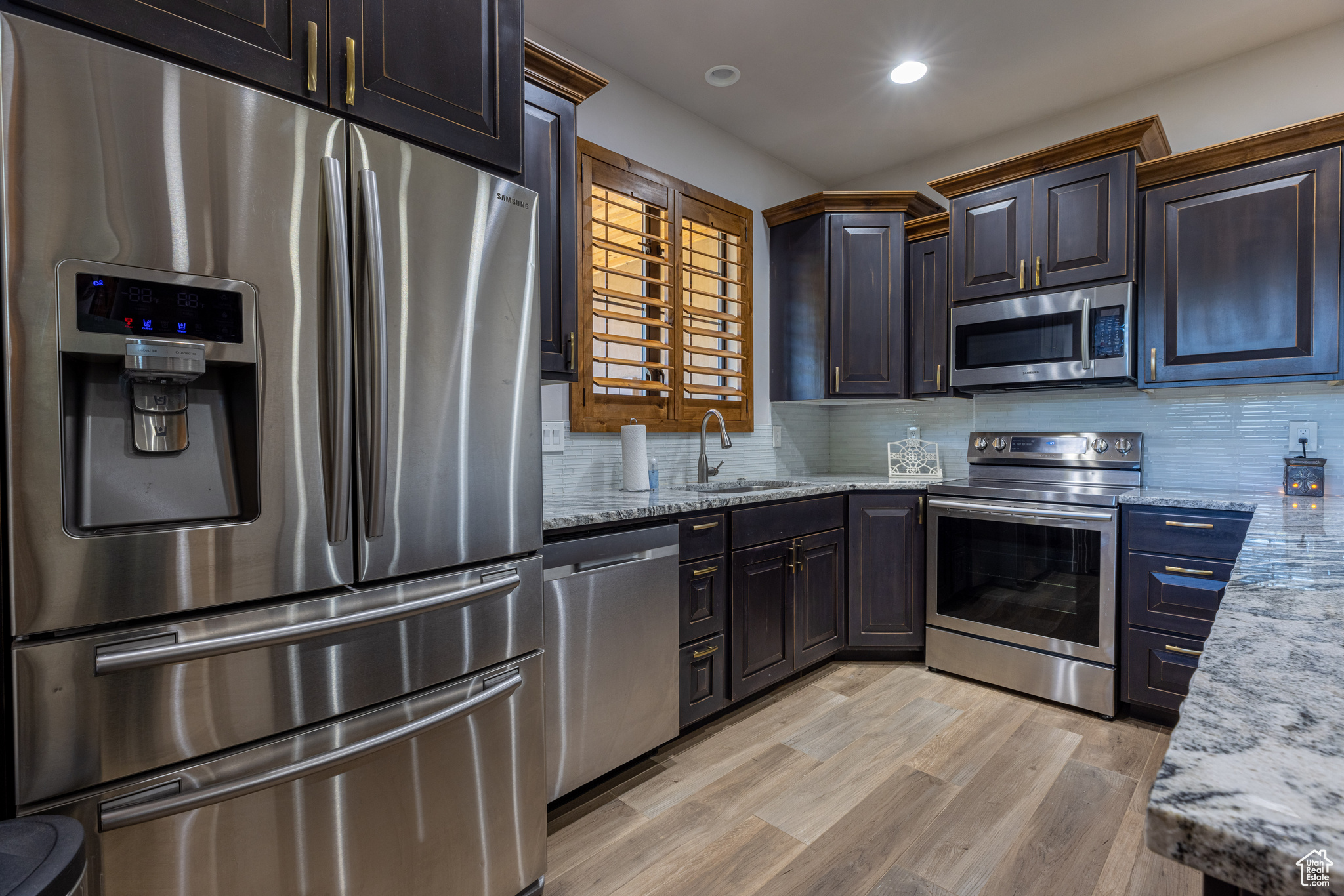 Guest casita featureing a full Kitchen with appliances with stainless steel finishes, sink, light stone counters, tasteful backsplash, and light hardwood / wood-style floors