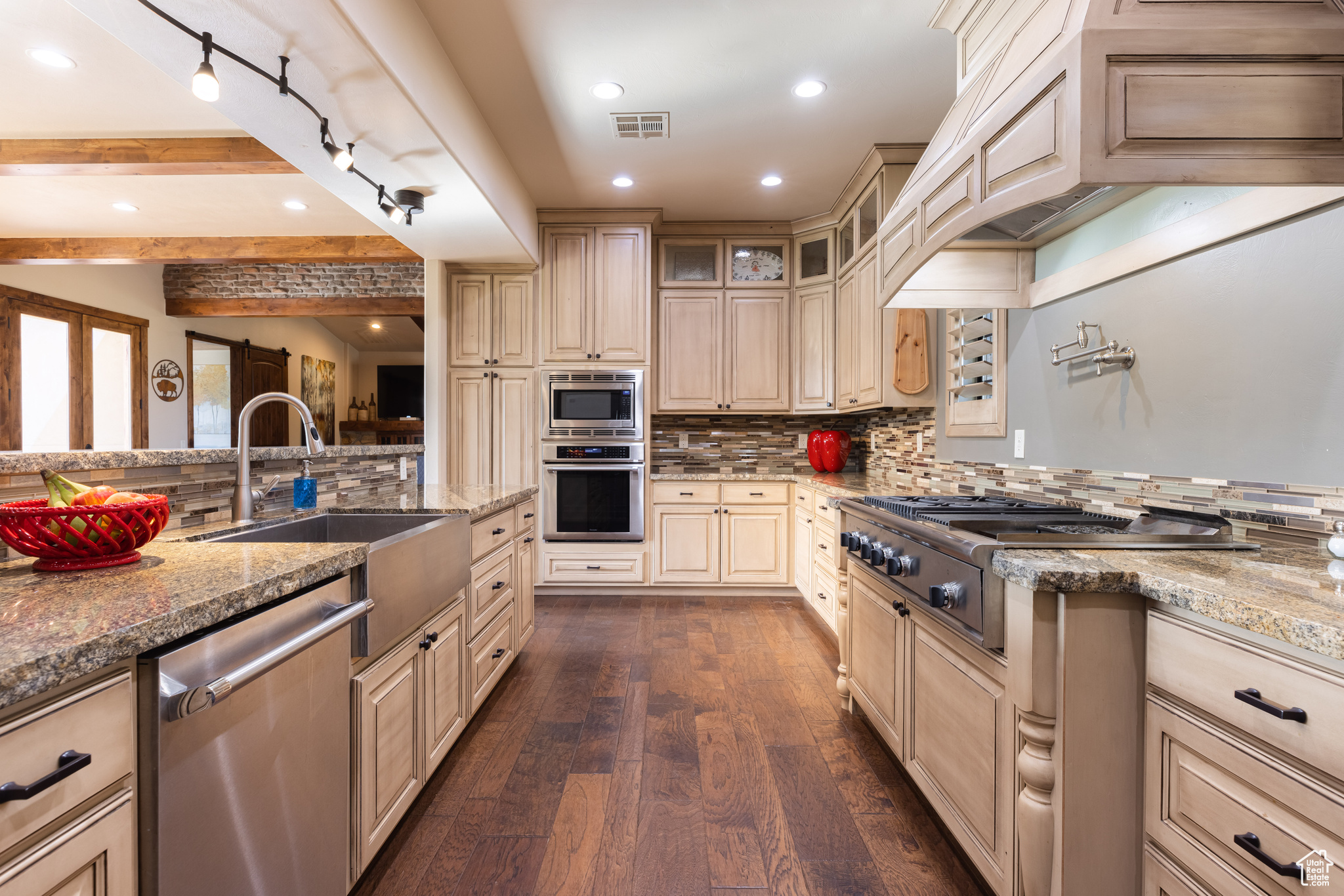 Kitchen with dark hardwood / wood-style floors, backsplash, beam ceiling, stainless steel appliances, and light stone counters