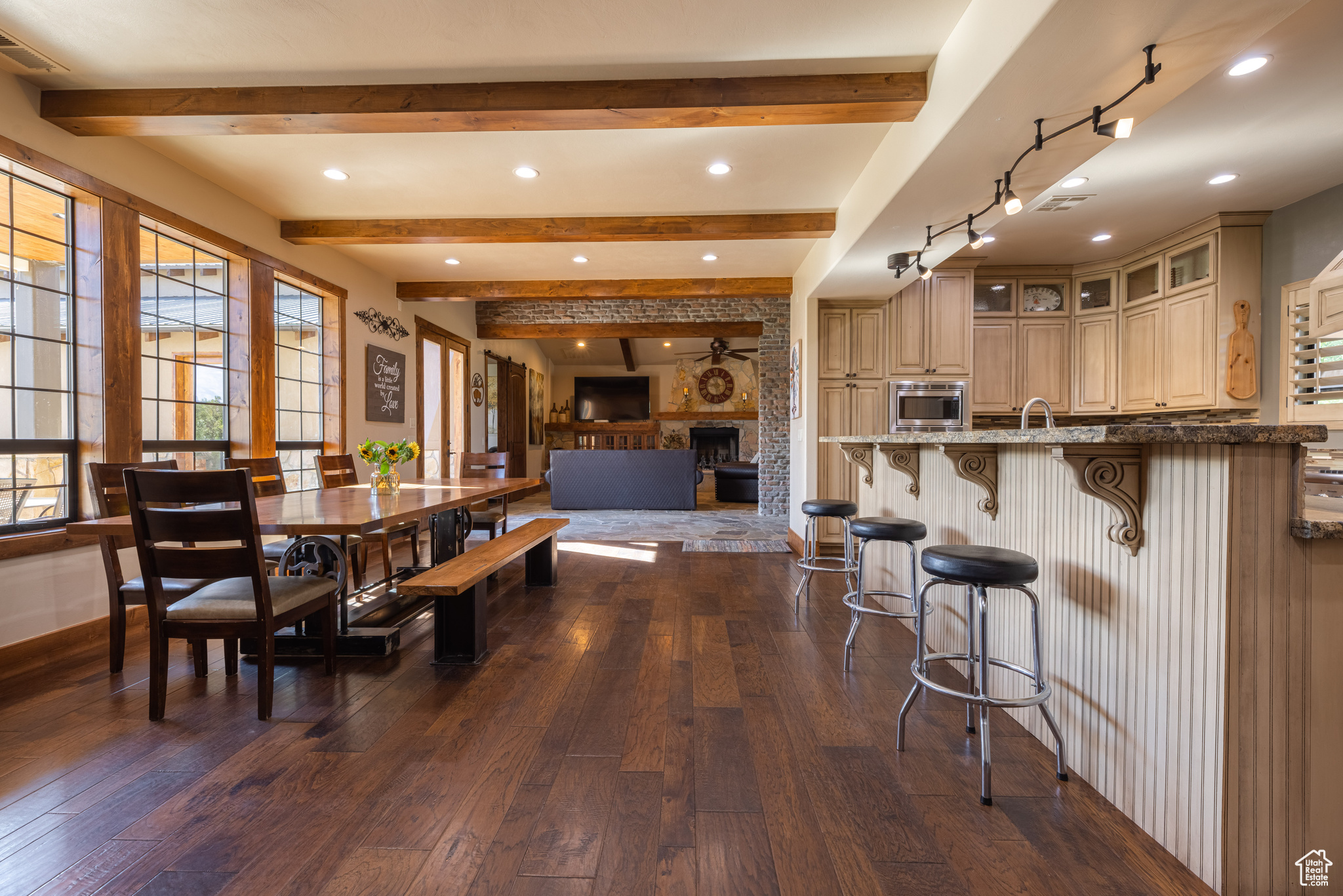 Dining area with beamed ceiling, sink, hardwood / wood-style flooring, and a stone fireplace