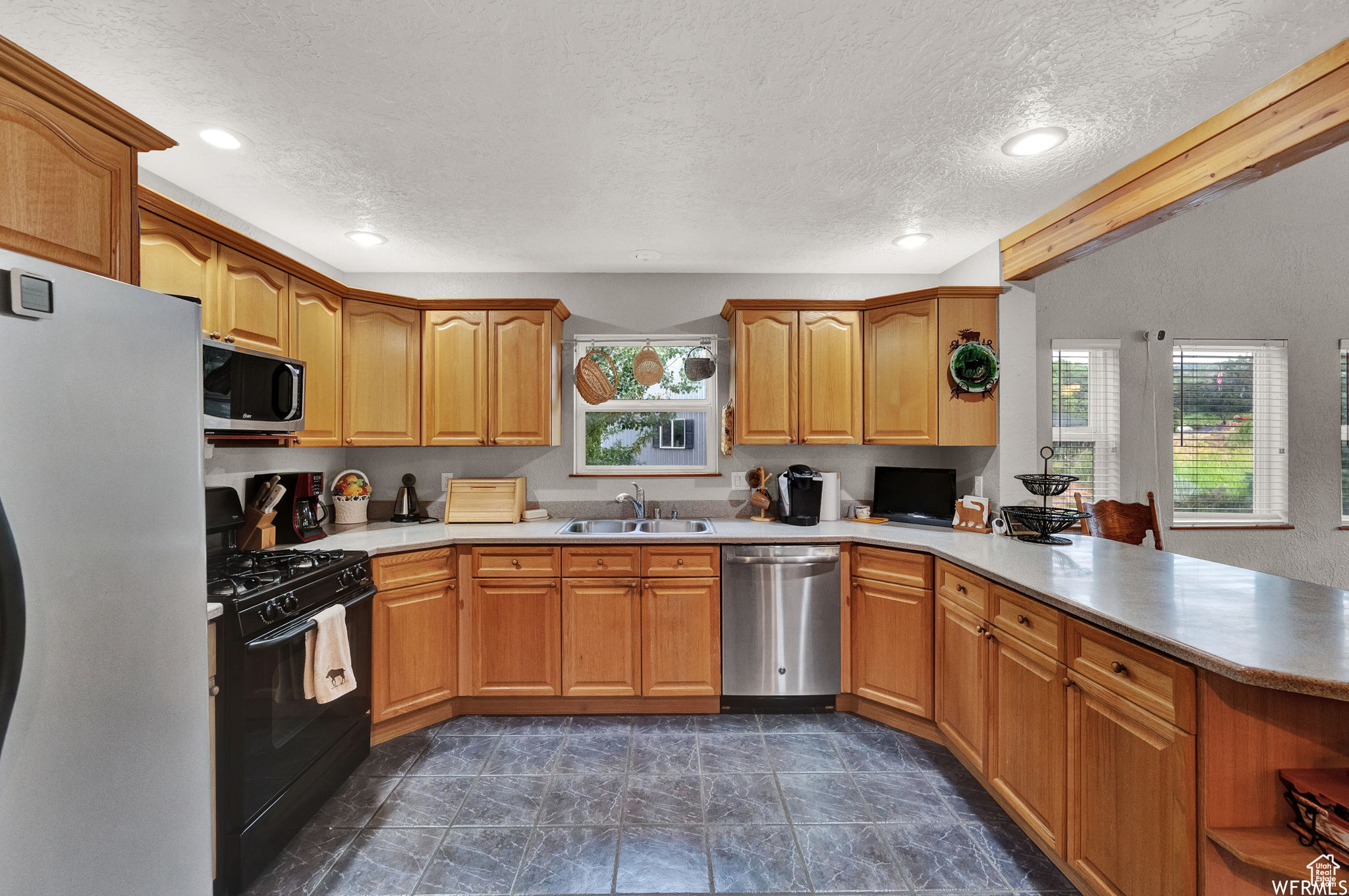 Kitchen with kitchen peninsula, stainless steel appliances, a textured ceiling, sink, and dark tile floors