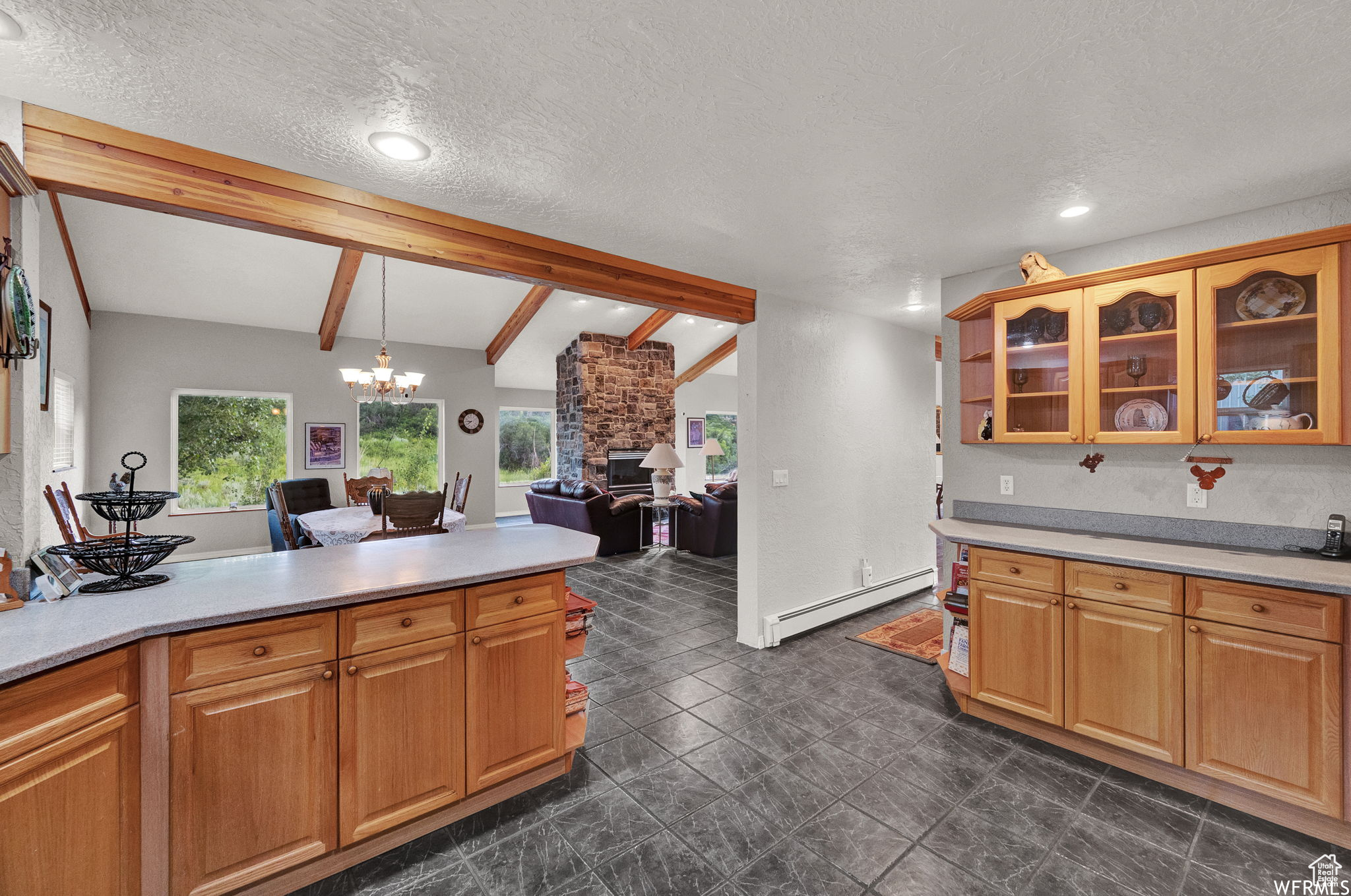 Kitchen with dark tile floors, a baseboard heating unit, a stone fireplace, lofted ceiling with beams, and a textured ceiling