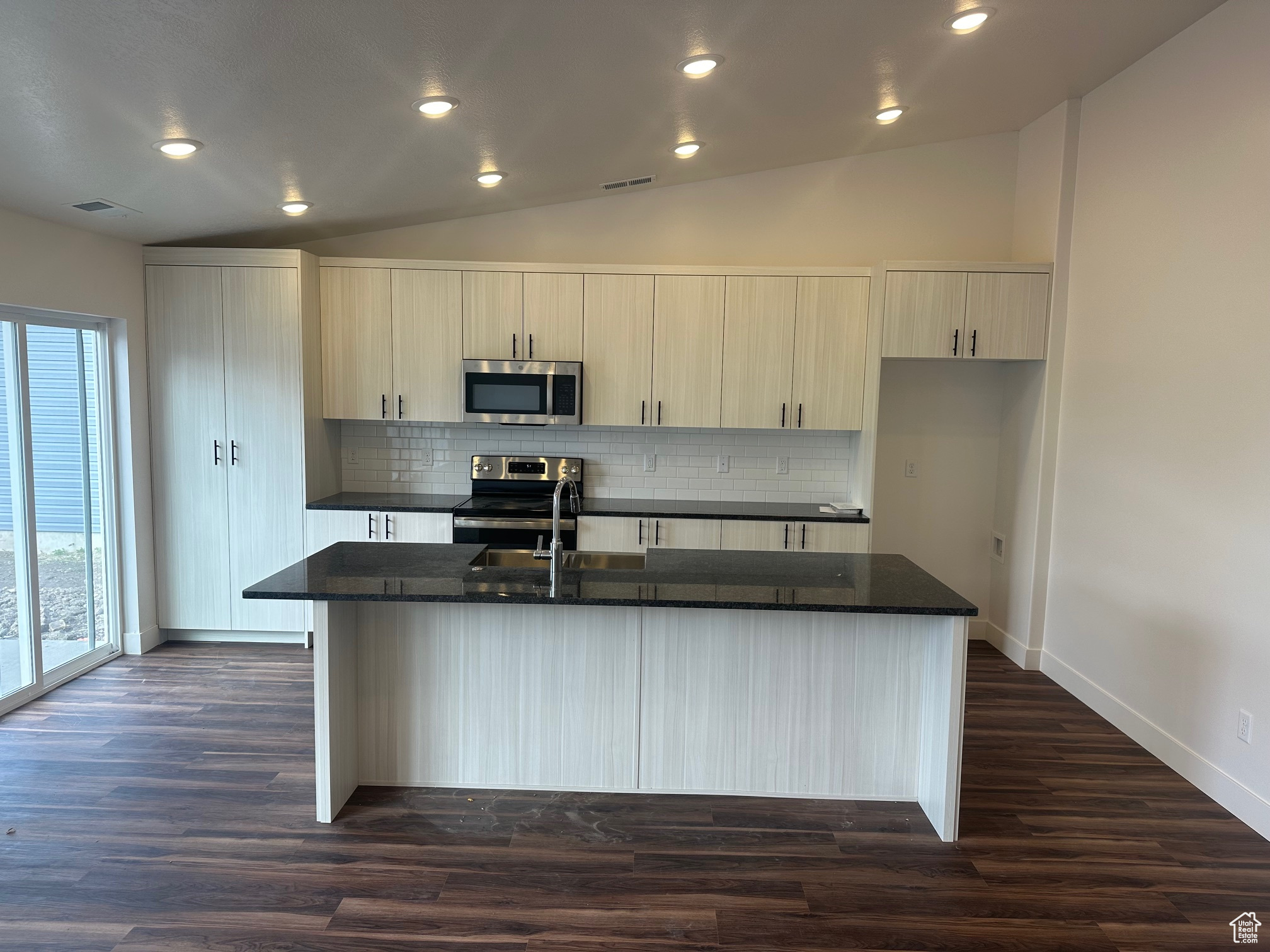 Kitchen with an island with sink, dark wood-type flooring, lofted ceiling, and appliances with stainless steel finishes