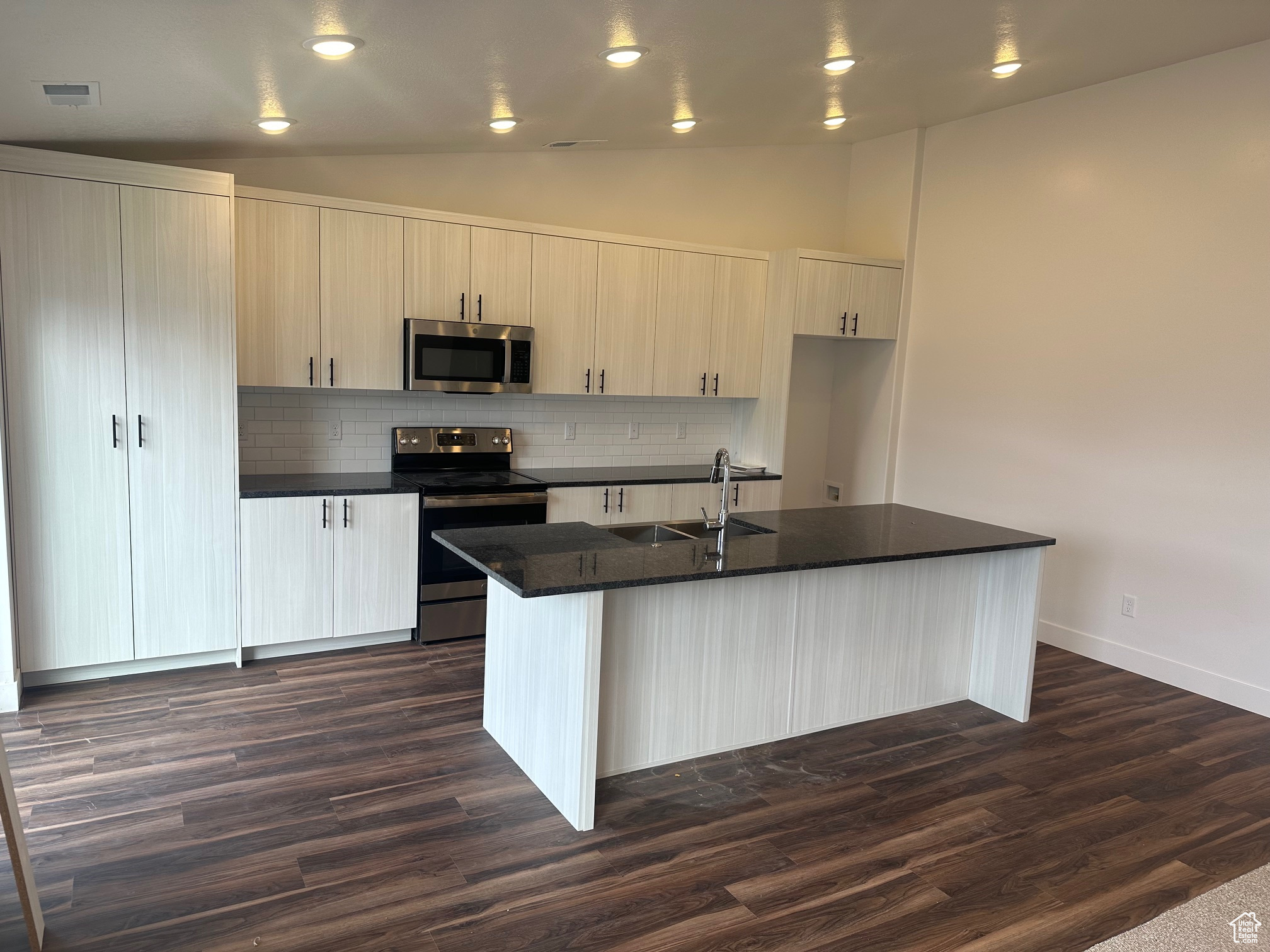 Kitchen featuring stainless steel appliances, dark hardwood / wood-style flooring, an island with sink, and tasteful backsplash