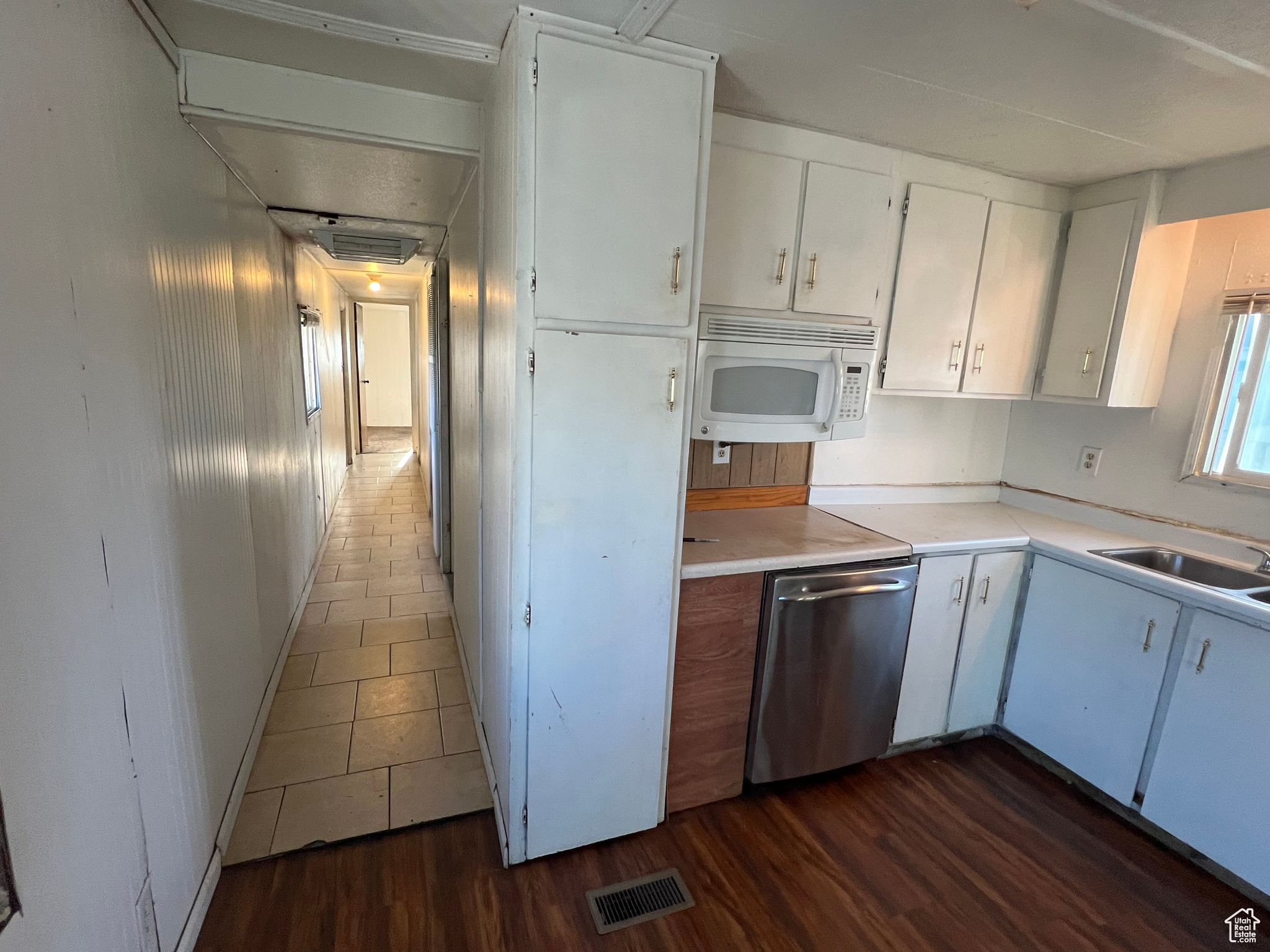 Kitchen featuring white cabinets, sink, dark tile floors, and stainless steel dishwasher