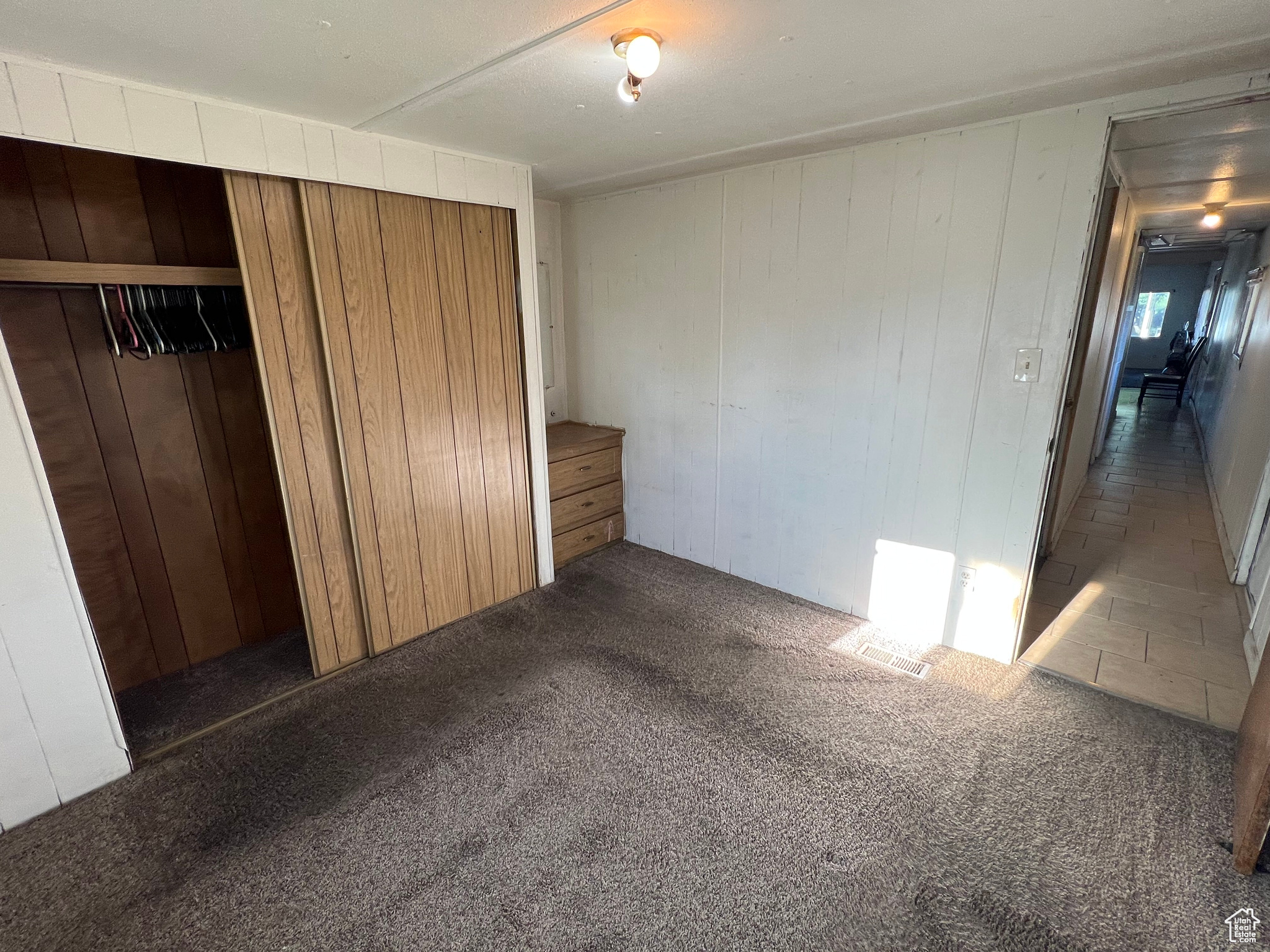 Unfurnished bedroom with wood walls, dark carpet, and a closet