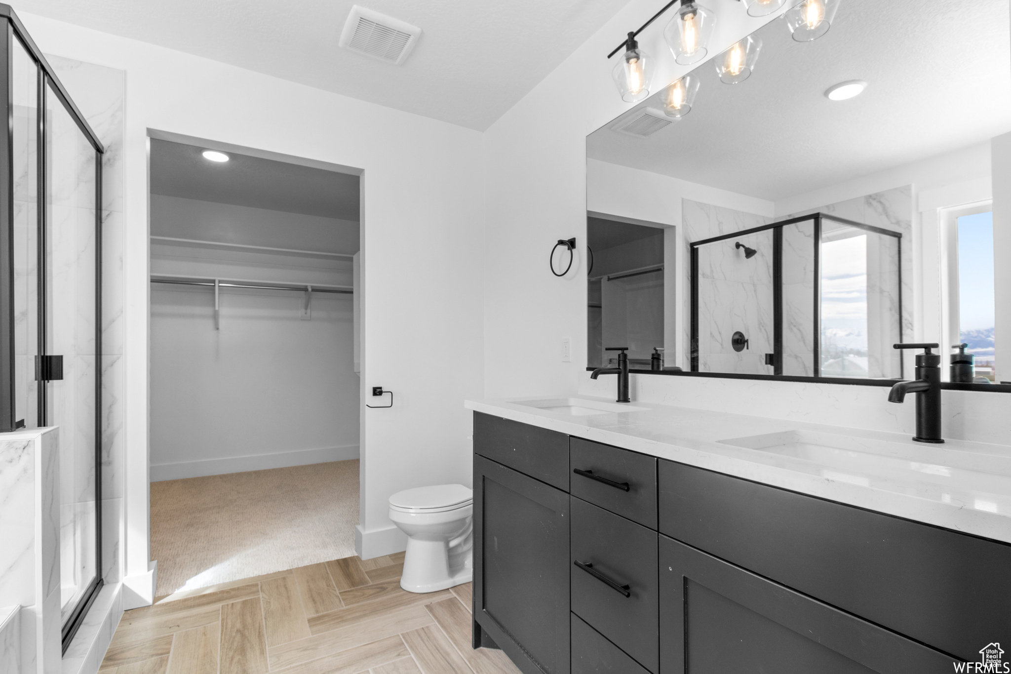 Bathroom featuring walk in shower, toilet, double sink vanity, and parquet flooring