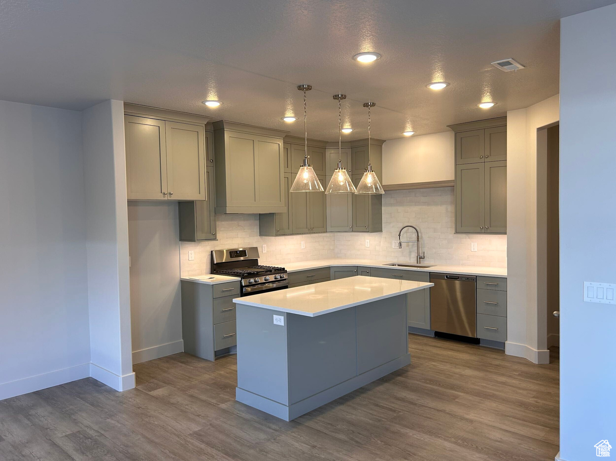Kitchen featuring a kitchen island, stainless steel appliances, decorative light fixtures, wood-type flooring, and sink