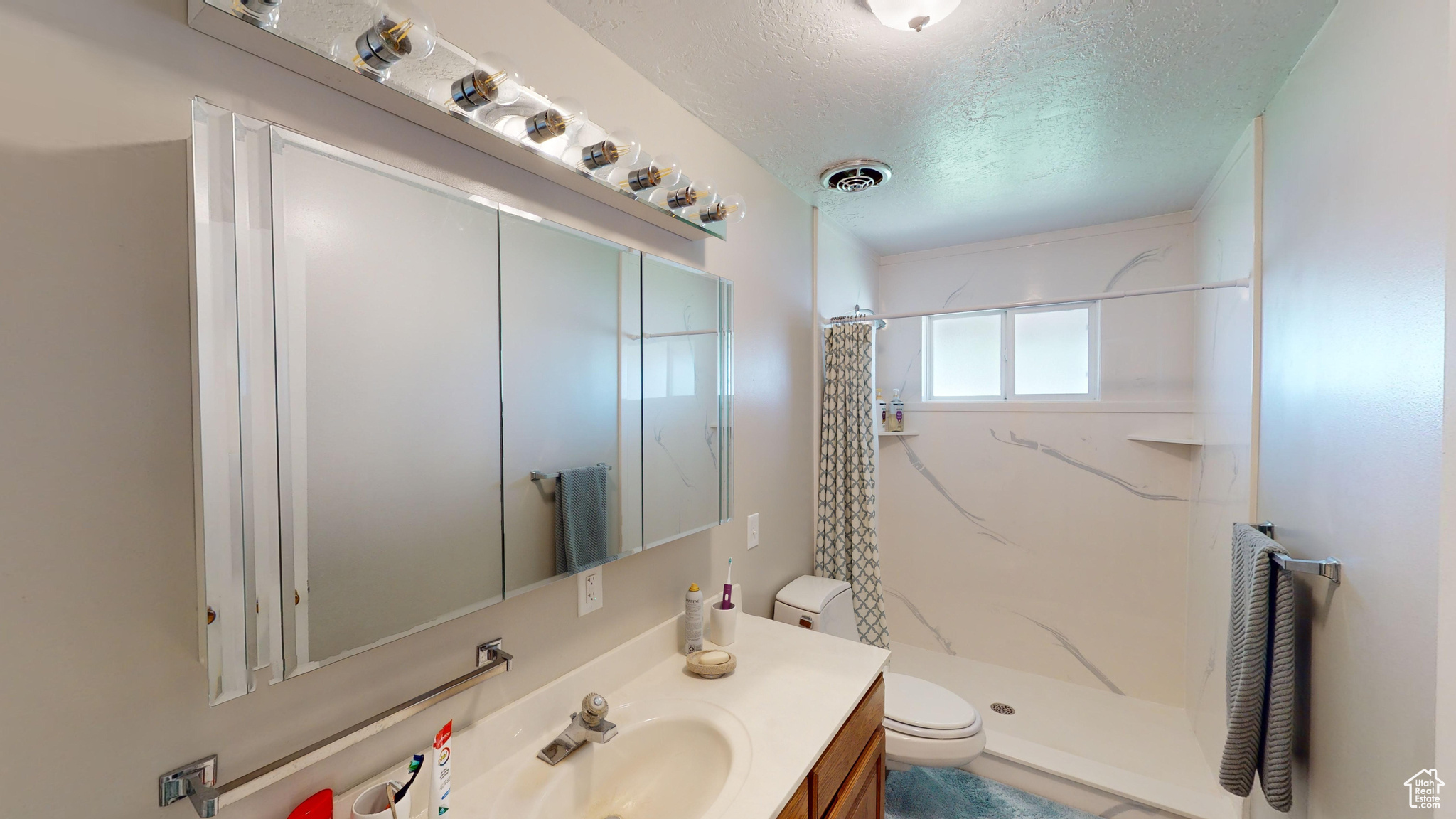 Bathroom featuring a shower with shower curtain, vanity with extensive cabinet space, toilet, and a textured ceiling