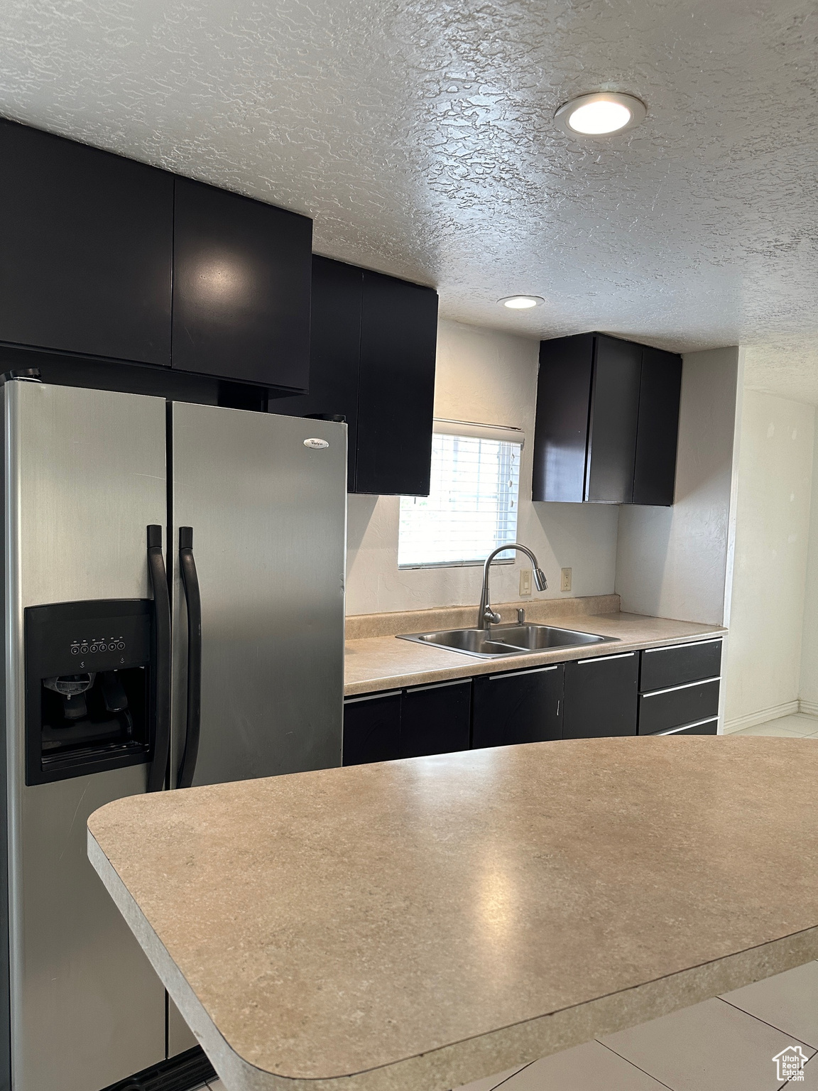 Kitchen with a textured ceiling, sink, and stainless steel fridge