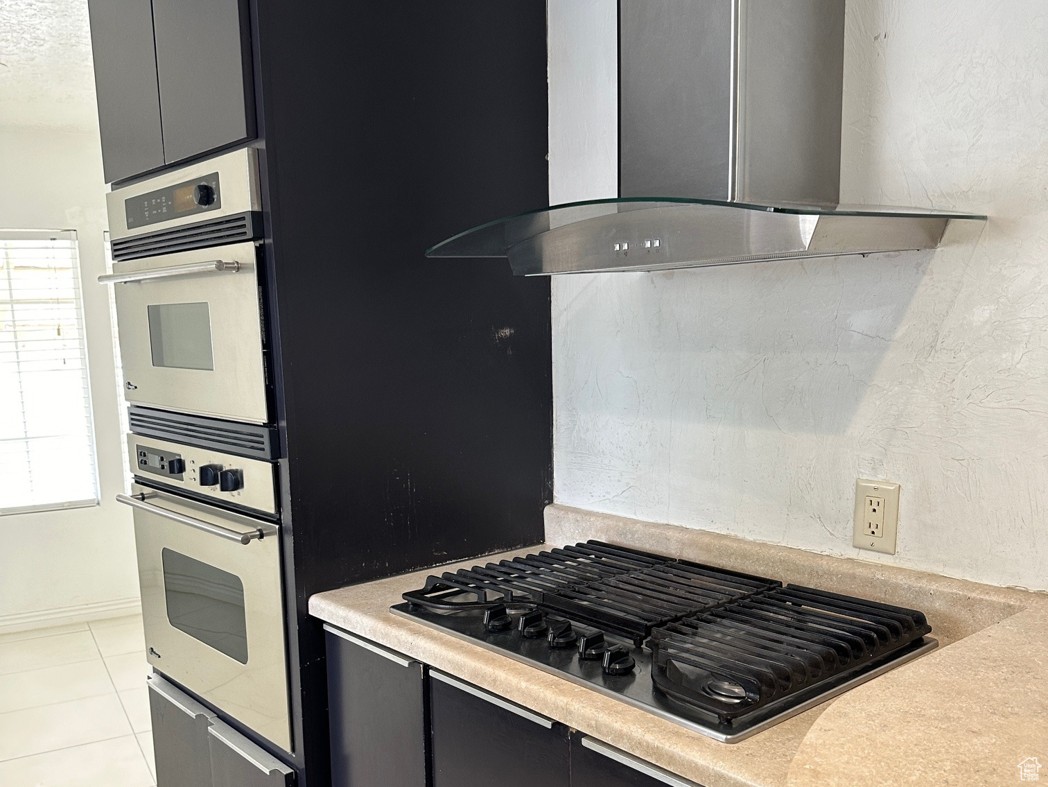 Kitchen featuring appliances with stainless steel finishes, wall chimney exhaust hood, and light tile floors