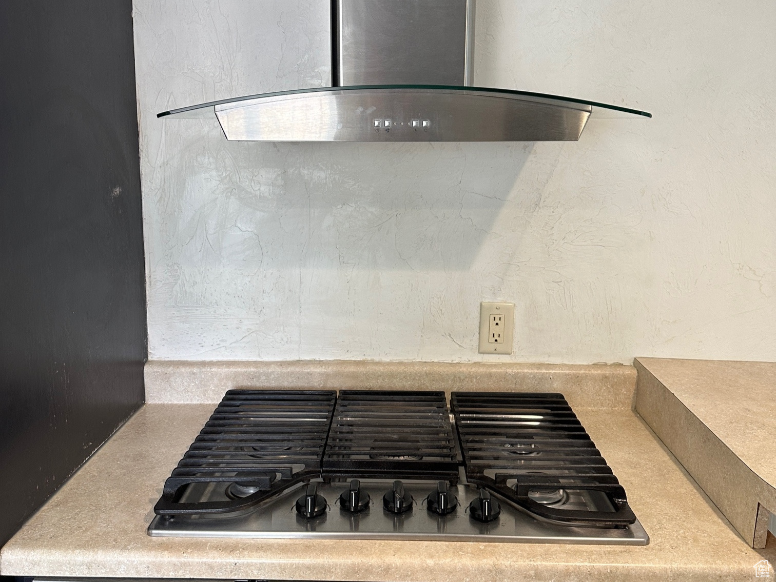 Kitchen with wall chimney range hood and stainless steel gas cooktop