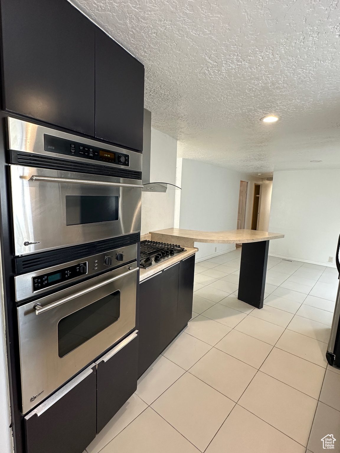 Kitchen with a textured ceiling, light tile floors, and stainless steel appliances