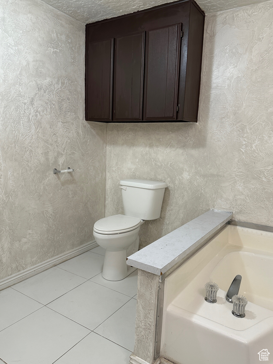 Bathroom with tile floors, a washtub, a textured ceiling, and toilet