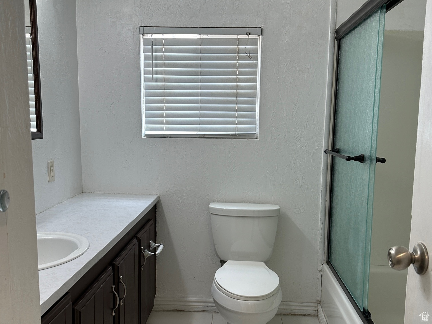 Full bathroom featuring tile flooring, a textured ceiling, enclosed tub / shower combo, vanity, and toilet