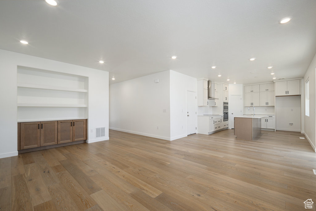 Unfurnished living room with sink, light hardwood / wood-style flooring, and built in shelves