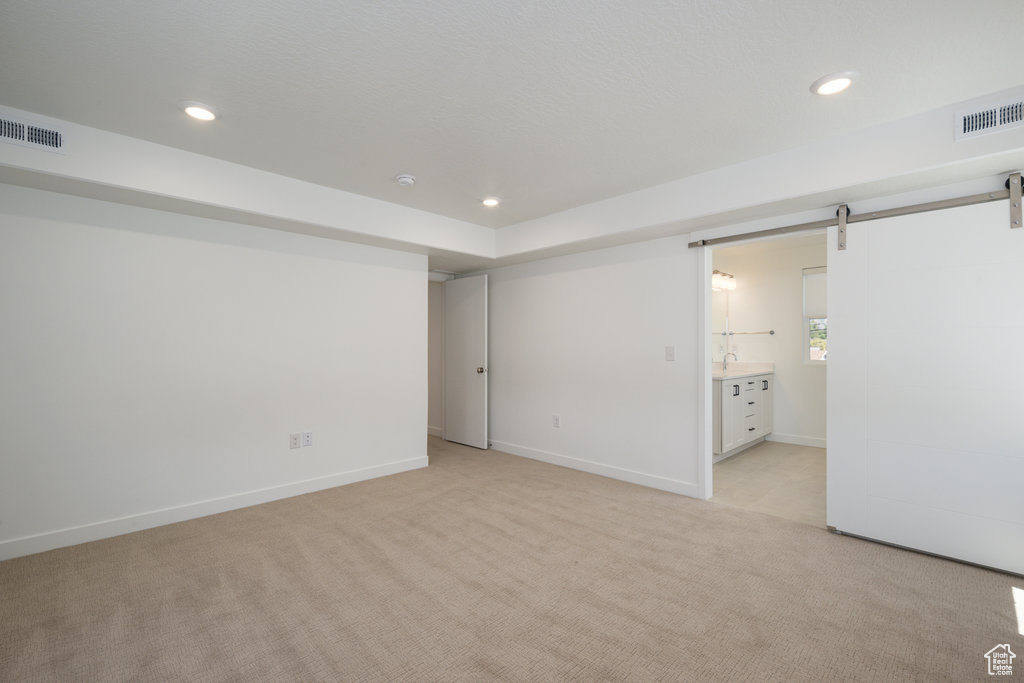 Unfurnished bedroom featuring a barn door, light colored carpet, and ensuite bathroom