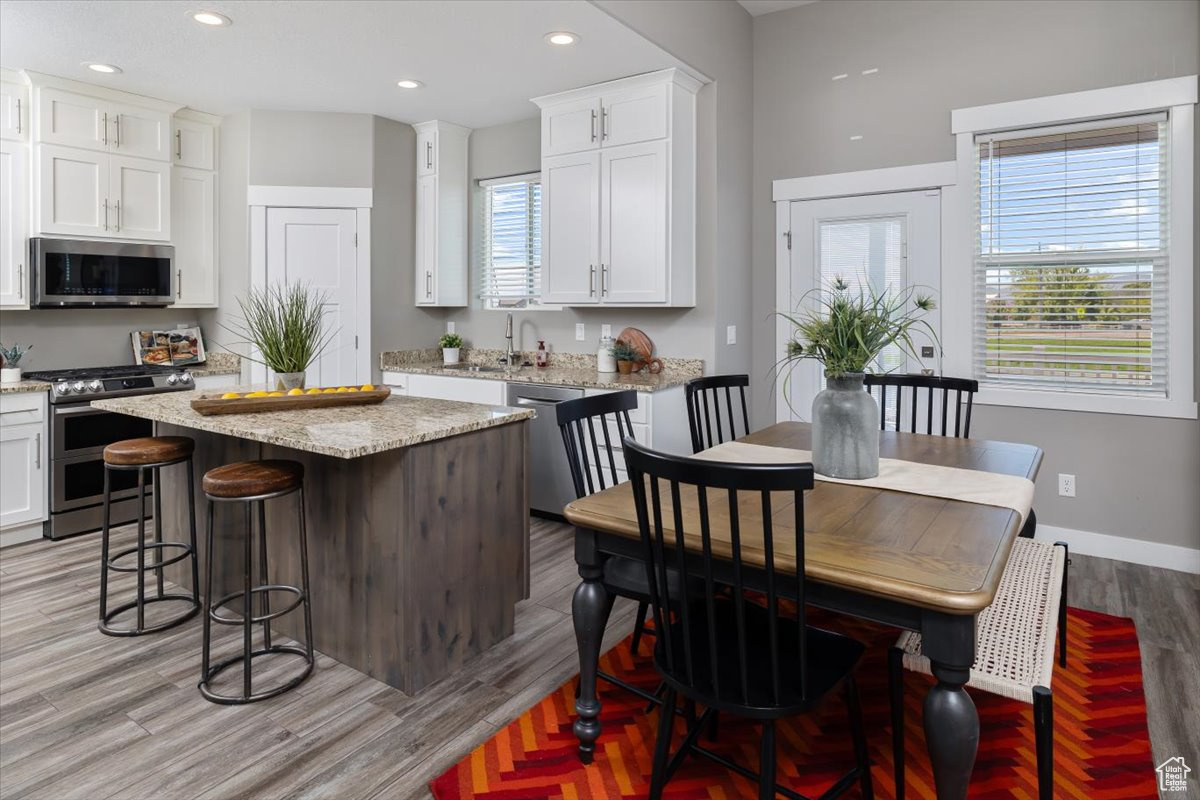 Kitchen featuring light hardwood / wood-style floors, white cabinets, a kitchen island, and appliances with stainless steel finishes