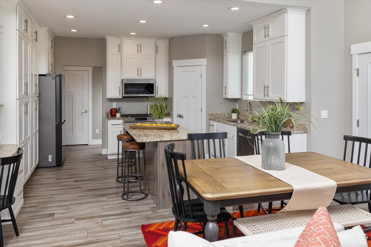 Kitchen featuring white cabinetry, light stone countertops, light hardwood / wood-style flooring, stainless steel appliances, and sink