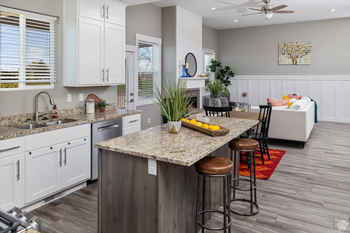 Kitchen featuring a center island, white cabinetry, wood-type flooring, a large fireplace, and ceiling fan