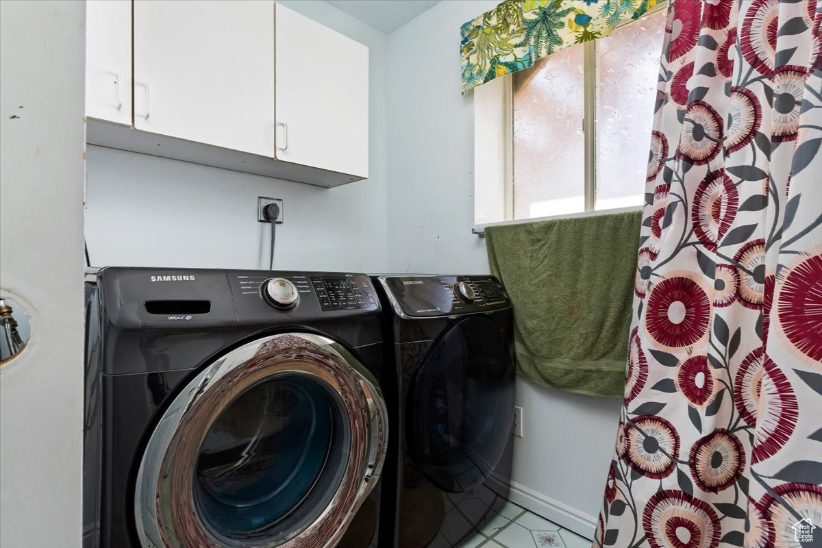 Laundry area with independent washer and dryer, tile flooring, hookup for an electric dryer, and cabinets