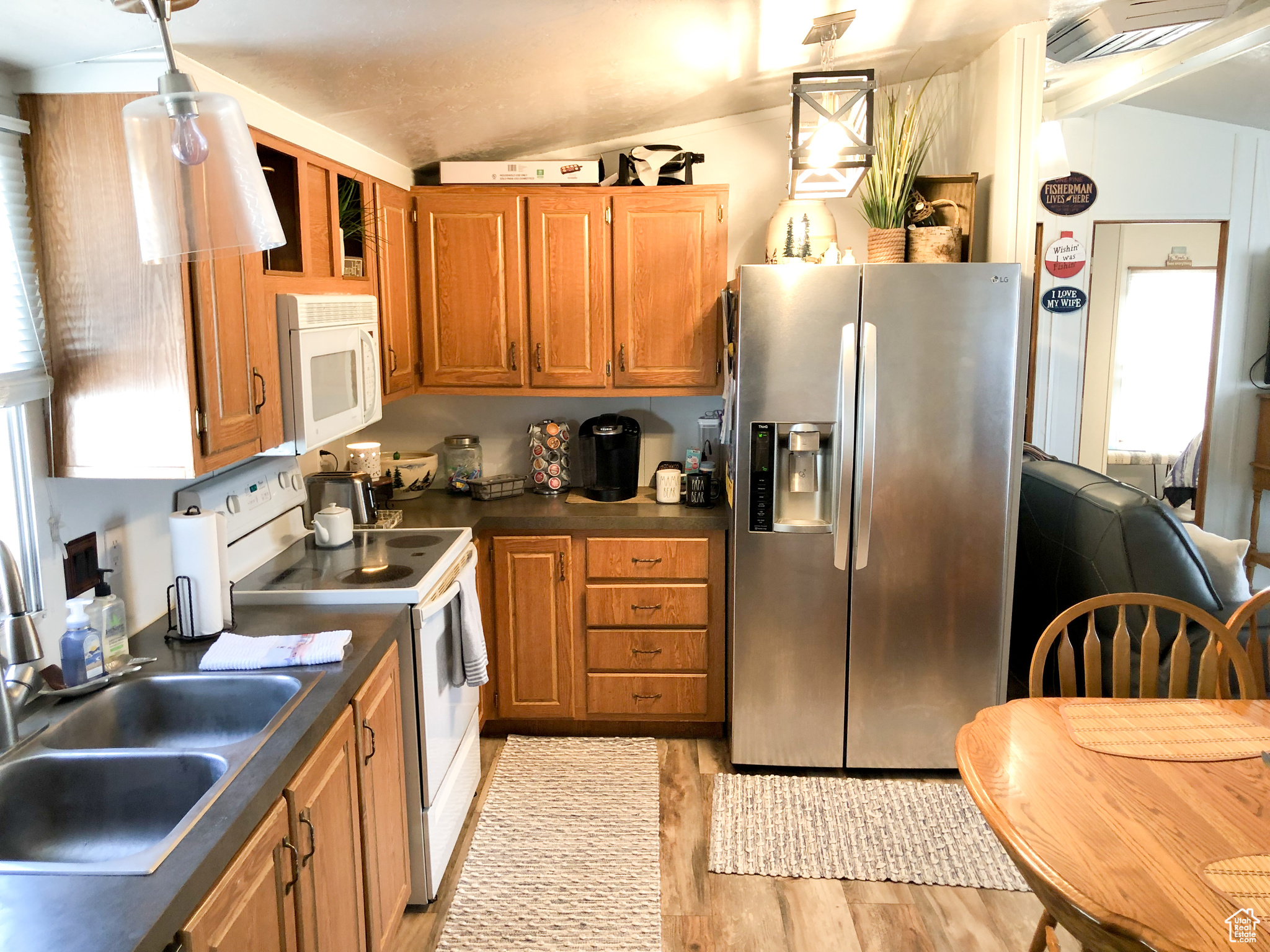 Kitchen with light hardwood / wood-style flooring, white appliances, hanging light fixtures, sink, and lofted ceiling