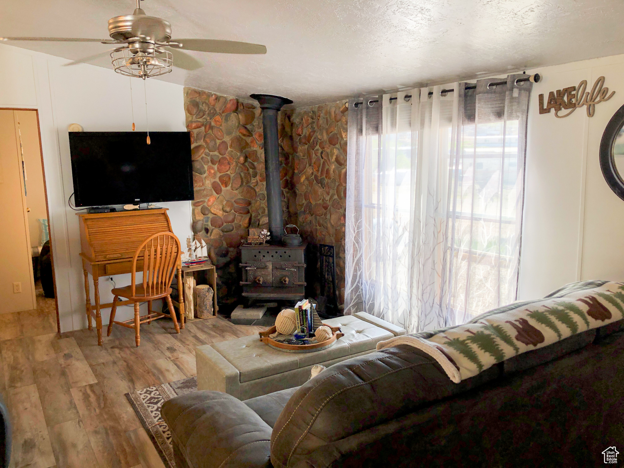 Living room featuring ceiling fan, hardwood / wood-style flooring, a wood stove, and a textured ceiling