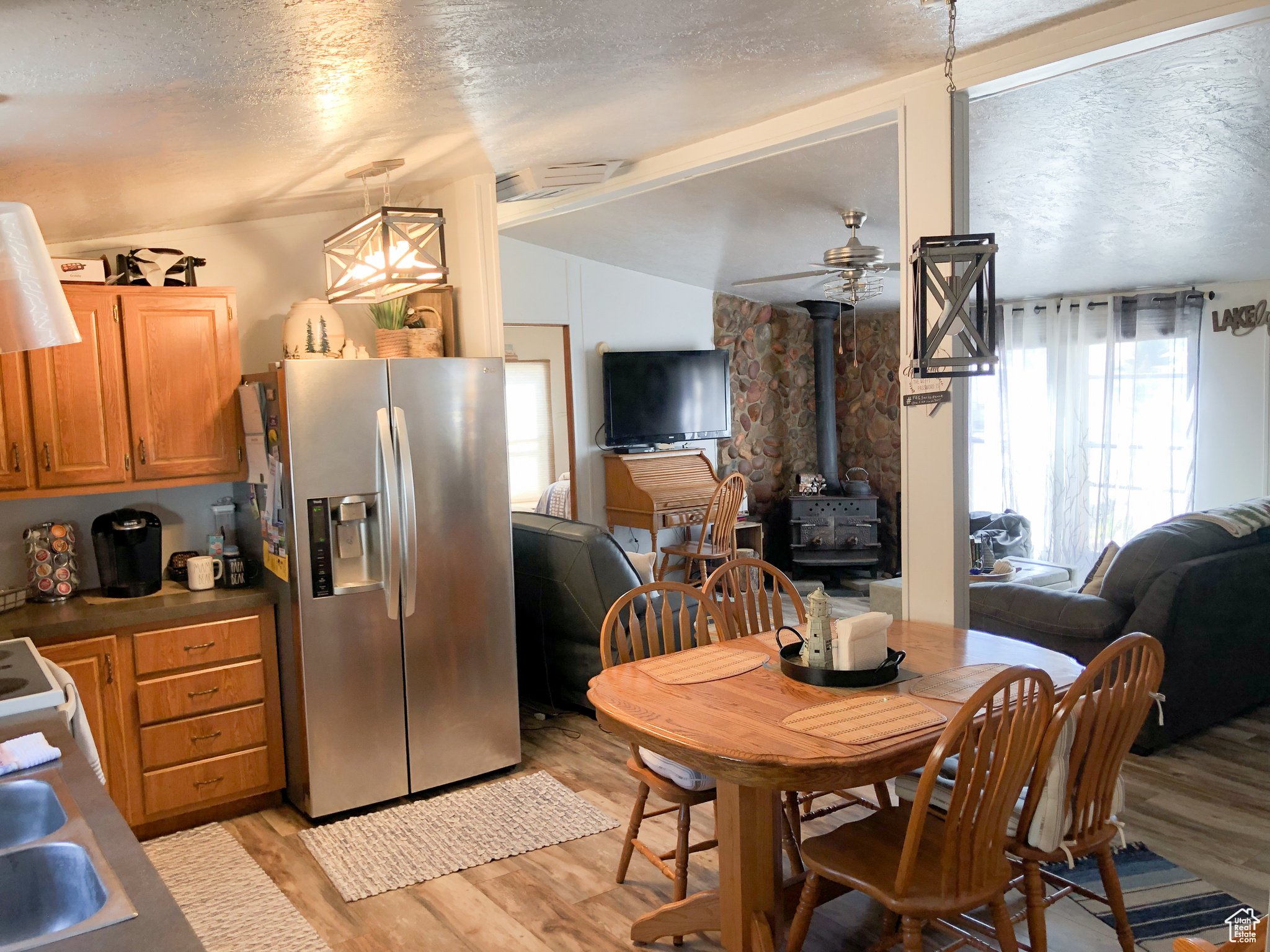 Dining room with a textured ceiling, light hardwood / wood-style flooring, a wood stove, ceiling fan, and vaulted ceiling