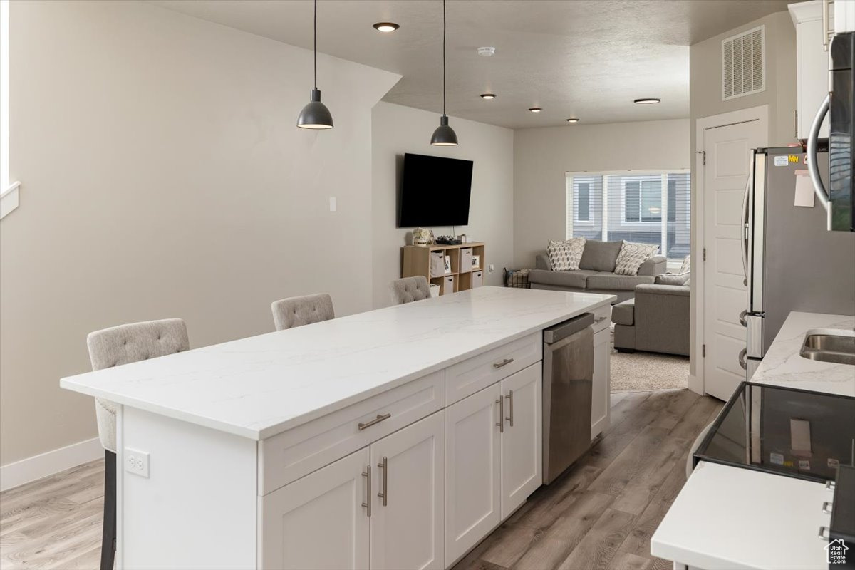 Kitchen with a kitchen breakfast bar, white cabinetry, light hardwood / wood-style flooring, and pendant lighting