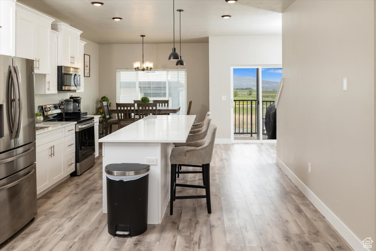 Kitchen with stainless steel appliances, decorative light fixtures, light wood-type flooring, a center island, and white cabinetry