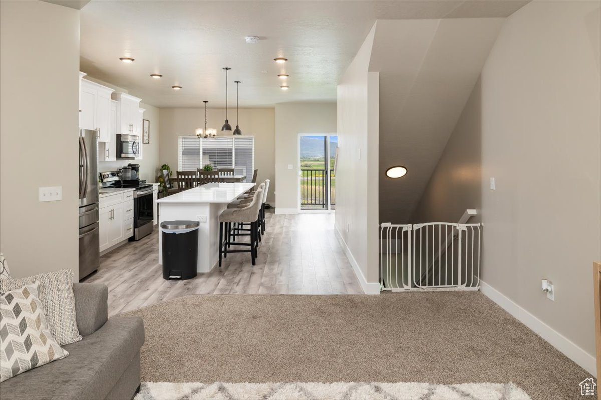 Kitchen featuring decorative light fixtures, stainless steel appliances, a breakfast bar area, a center island, and white cabinets