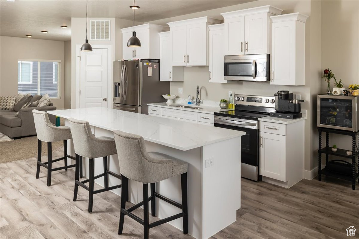 Kitchen featuring stainless steel appliances, light wood-type flooring, pendant lighting, a center island, and white cabinetry