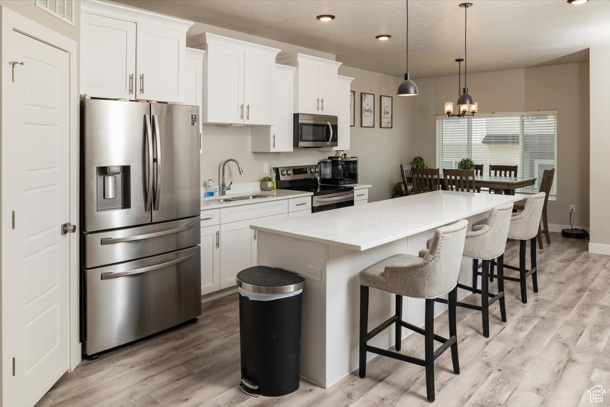 Kitchen featuring decorative light fixtures, a kitchen island, stainless steel appliances, light wood-type flooring, and sink