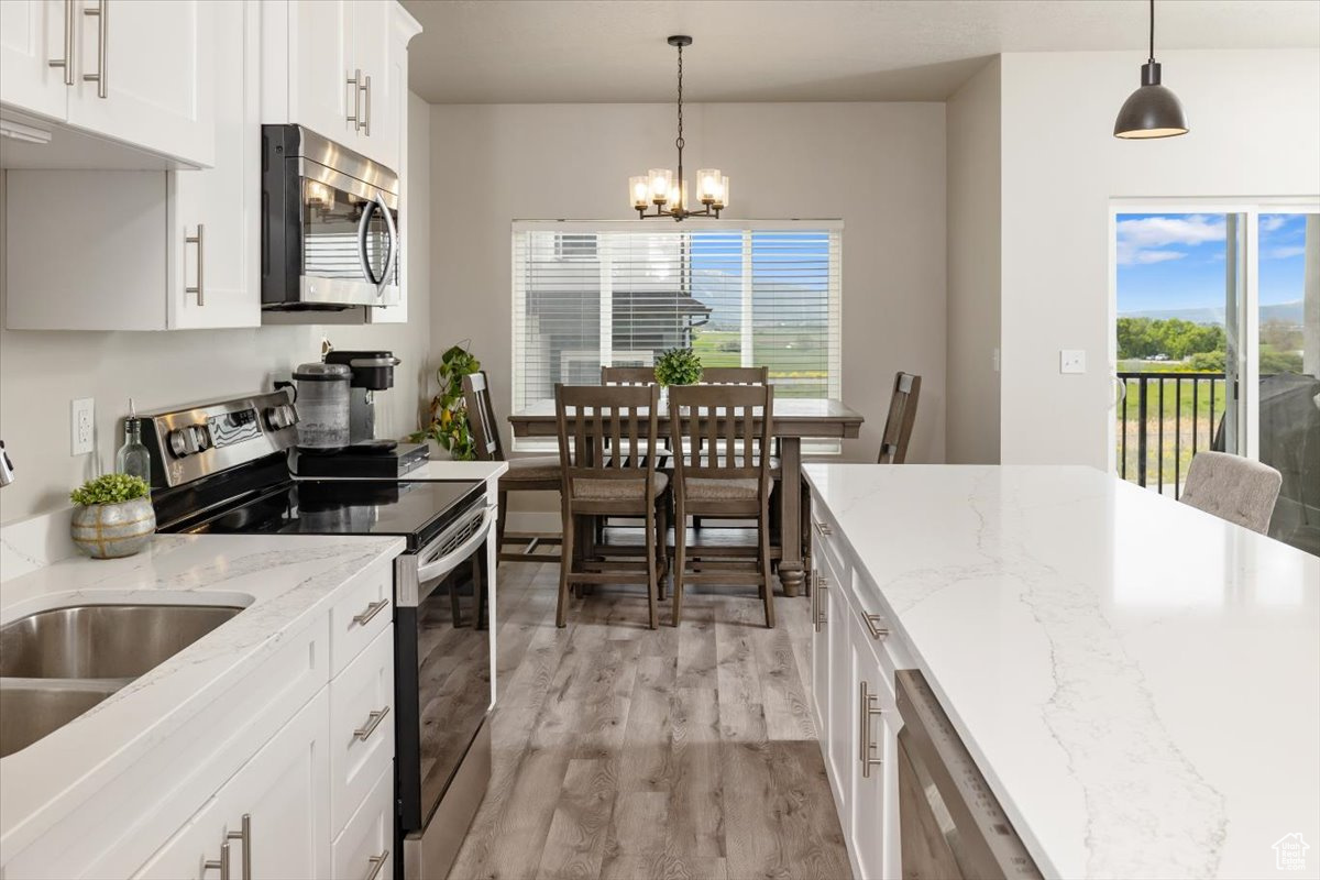 Kitchen with stainless steel appliances, light hardwood / wood-style floors, white cabinets, and decorative light fixtures