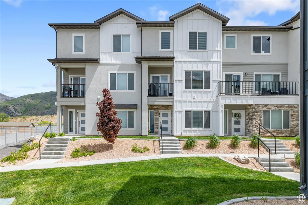 View of property with a front yard, a mountain view, and a balcony