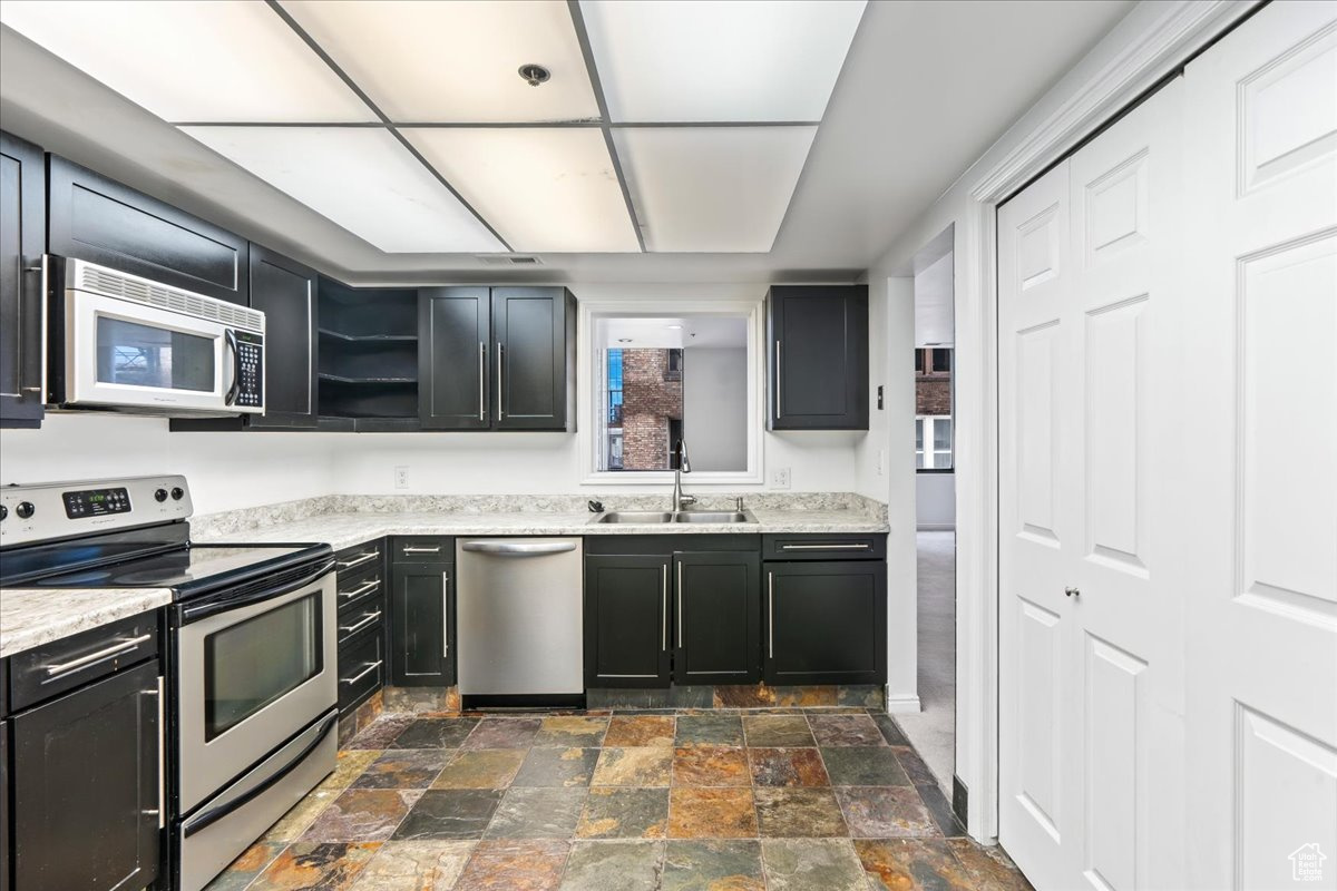 Kitchen featuring appliances with stainless steel finishes, light stone counters, sink, and dark tile floors