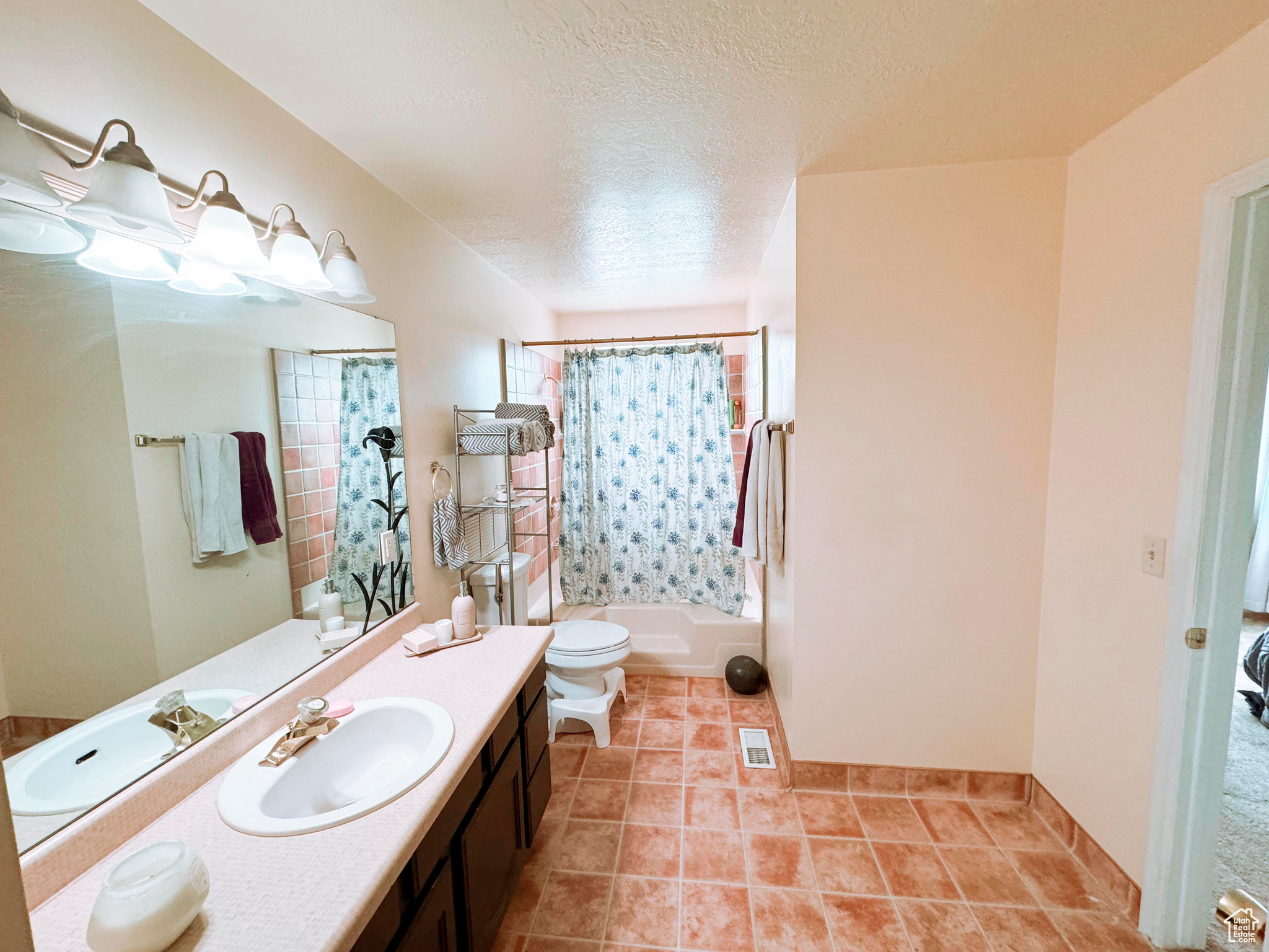 Full bathroom featuring tile flooring, shower / bath combination with curtain, a textured ceiling, toilet, and vanity