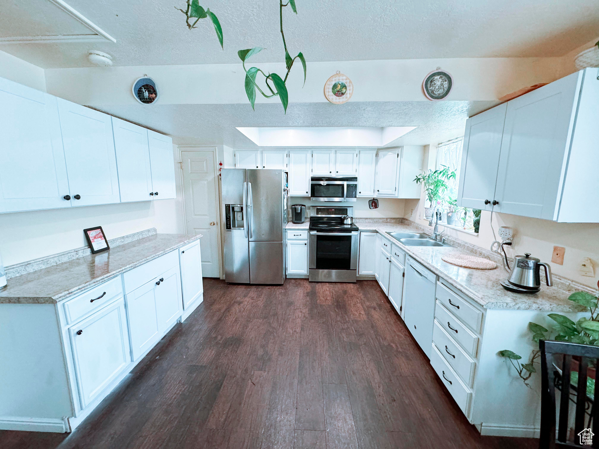 Kitchen with white cabinetry, light stone countertops, dark wood-type flooring, appliances with stainless steel finishes, and sink